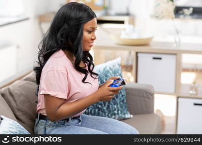 people and leisure concept - happy smiling african american young woman with gamepad playing video game at home. african american woman with gamepad playing game