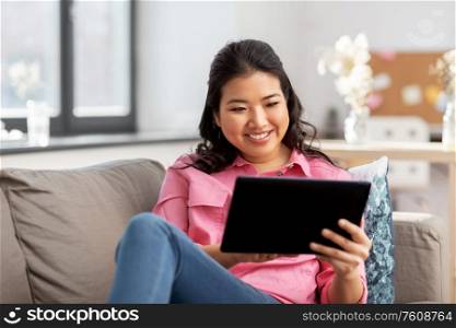 people and leisure concept - happy smiling asian young woman in pink shirt with tablet pc computer sitting on sofa at home. asian young woman with tablet pc computer at home