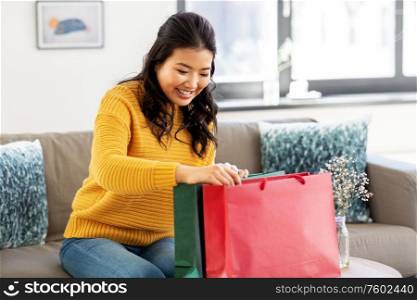 people and leisure concept - happy smiling asian young woman in yellow sweater with shopping bag sitting on sofa at home. asian young woman with shopping bag at home