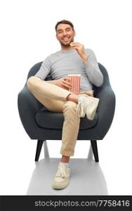 people and leisure concept - happy smiling man eating popcorn sitting in chair over white background. smiling man eating popcorn sitting in chair