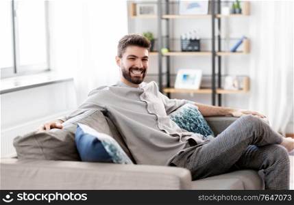 people and leisure concept - happy smiling man sitting on sofa at home. happy smiling man sitting on sofa at home