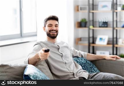 people and leisure concept - happy smiling man with remote control watching tv at home. happy man with remote control watching tv at home