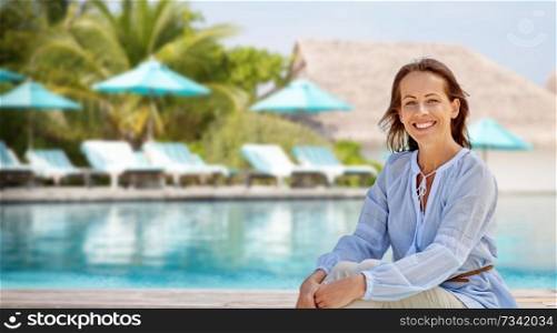 people and leisure concept - happy smiling woman over swimming pool of touristic resort background. happy woman over swimming pool of touristic resort