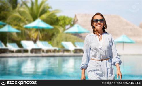 people and leisure concept - happy smiling woman walking over swimming pool of touristic resort background. happy woman over swimming pool of touristic resort