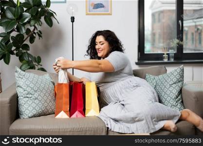 people and leisure concept - happy smiling young woman with shopping bags on sofa at home. happy young woman with shopping bags at home