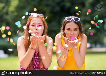people and leisure concept - happy teenage girls or friends blowing confetti off hands at summer park. teenage girls blowing confetti off hands in park