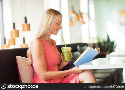 people and leisure concept - happy woman drinking green smoothie or vegetarian shake and reading book at restaurant or cafe. woman with drink reading book at cafe