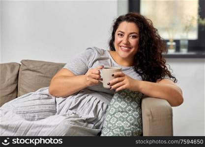 people and leisure concept - happy young woman drinking coffee or tea on sofa at home. happy woman drinking coffee or tea on sofa at home