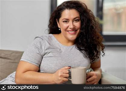 people and leisure concept - happy young woman drinking coffee or tea on sofa at home. happy woman drinking coffee or tea on sofa at home