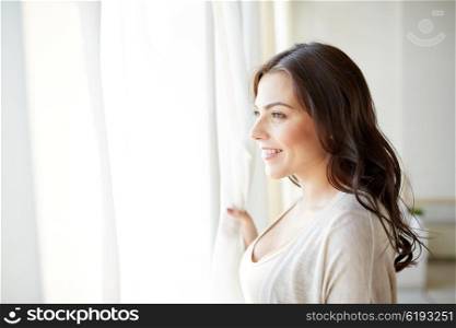 people and leisure concept - happy young woman looking through window at home. happy young woman looking through window at home