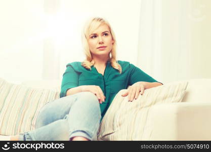 people and leisure concept - happy young woman sitting on sofa at home. happy young woman at home