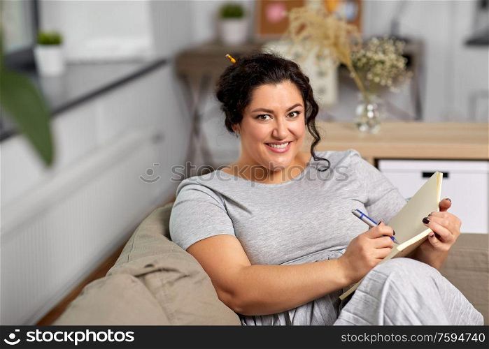 people and leisure concept - happy young woman with diary and pen taking notes on sofa at home. happy young woman with diary on sofa at home