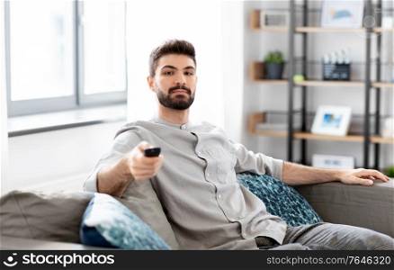 people and leisure concept - man with remote control watching tv at home. man with remote control watching tv at home