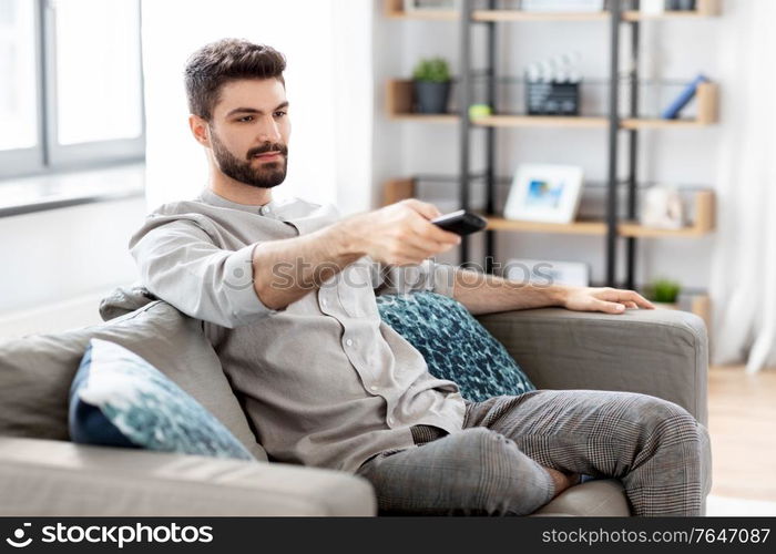 people and leisure concept - man with remote control watching tv at home. man with remote control watching tv at home