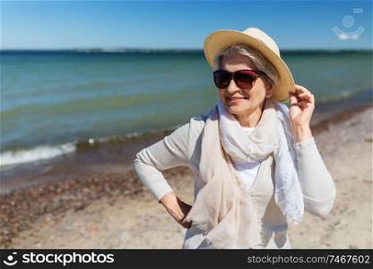 people and leisure concept - portrait of happy senior woman in sunglasses and straw hat on beach in estonia. happy senior woman in sunglasses and hat on beach
