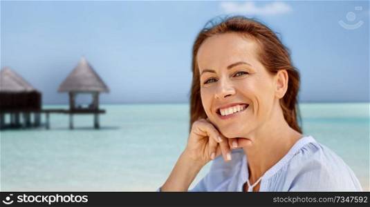 people and leisure concept - portrait of happy smiling woman over tropical beach and bungalow on maldives background. portrait of happy smiling woman on summer beach