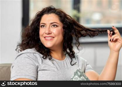 people and leisure concept - portrait of happy young woman playing with her hair strand at home. portrait of happy young woman at home