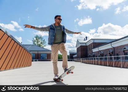 people and leisure concept - smiling indian man doing trick on skateboard on roof top. indian man doing trick on skateboard on roof top