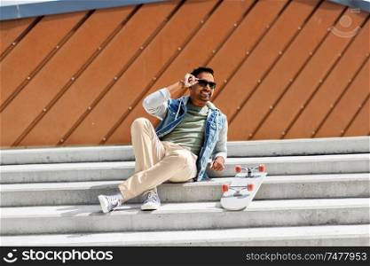 people and leisure concept - smiling indian man with skateboard sitting on stairs in city. indian man with skateboard sitting on city stairs