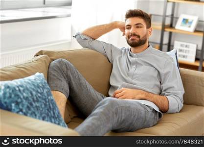 people and leisure concept - young man sitting on sofa at home. young man sitting on sofa at home