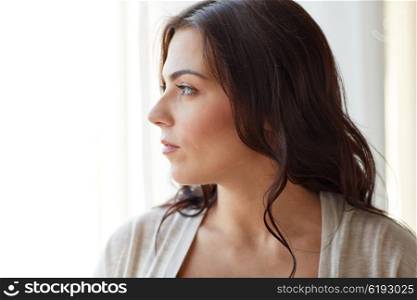 people and leisure concept - young woman looking through window at home. young woman looking through window at home