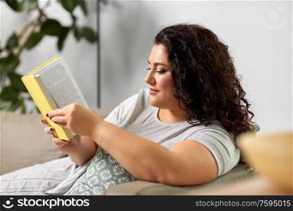 people and leisure concept - young woman reading book on sofa at home. young woman reading book on sofa at home
