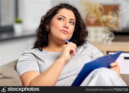 people and leisure concept - young woman with clipboard and pen thinking at home. woman with clipboard and pen thinking at home