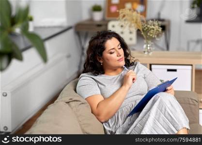 people and leisure concept - young woman with clipboard and pen thinking at home. woman with clipboard and pen thinking at home