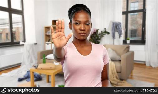 people and mess concept - african american young woman showing stop gesture over dirty room background. african american woman over dirty room background