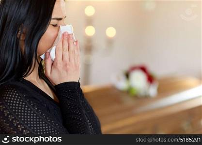 people and mourning concept - close up of crying woman with coffin at funeral in church. woman with coffin crying at funeral in church