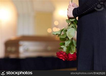 people and mourning concept - close up of woman with red roses and coffin at funeral in church. close up of woman with roses and coffin at funeral
