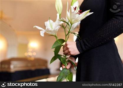 people and mourning concept - close up of woman with white lily flowers and coffin at funeral in church. close up of woman with lily flowers at funeral