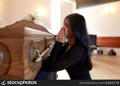people and mourning concept - crying woman with coffin at funeral in church. woman with coffin crying at funeral in church