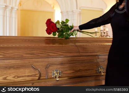 people and mourning concept - woman with red roses and coffin at funeral in church. woman with red roses and coffin at funeral