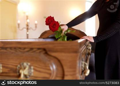 people and mourning concept - woman with red roses and coffin at funeral in church. woman with red roses and coffin at funeral