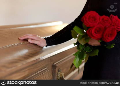 people and mourning concept - woman with red roses and coffin at funeral in church. woman with red roses and coffin at funeral