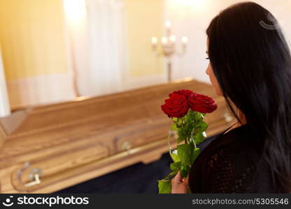 people and mourning concept - woman with red roses and coffin at funeral in church. woman with red roses and coffin at funeral