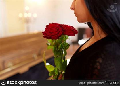 people and mourning concept - woman with red roses and coffin at funeral in church. woman with red roses and coffin at funeral