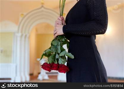 people and mourning concept - woman with red roses at funeral in orthodox church. woman with red roses at funeral in church