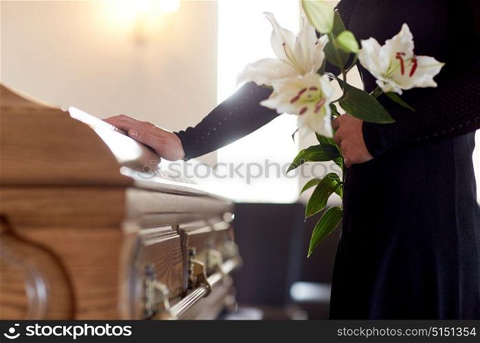 people and mourning concept - woman with white lily flowers and coffin at funeral in church. woman with lily flowers and coffin at funeral