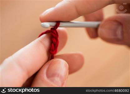 people and needlework concept - close up of hands knitting with crochet hook and red yarn. close up of hands knitting with crochet hook