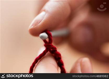 people and needlework concept - close up of hands knitting with crochet hook and red yarn. close up of hands knitting with crochet hook