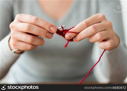people and needlework concept - woman hands knitting with crochet hook and red yarn. woman knitting with crochet hook and red yarn