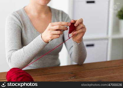 people and needlework concept - woman knitting with crochet hook and red yarn. woman knitting with crochet hook and red yarn