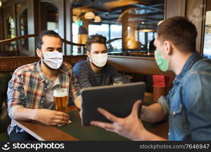 people and pandemic concept - male friends with tablet pc computer drinking beer at bar or pub. men in masks with tablet pc drink beer at bar