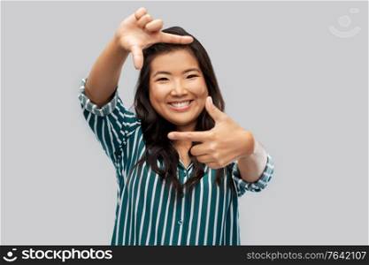 people and photography concept - happy smiling asian woman making frame of fingers over grey background. happy asian woman making frame of fingers