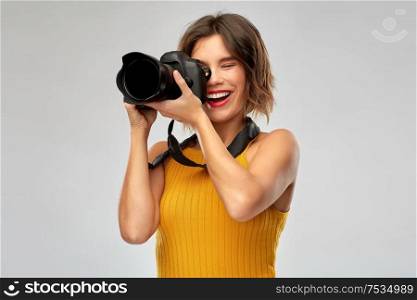 people and photography concept - happy woman photographer in mustard yellow top with digital camera over grey background. happy woman photographer with digital camera
