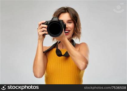 people and photography concept - happy woman photographer in mustard yellow top with digital camera over grey background. happy woman photographer with digital camera