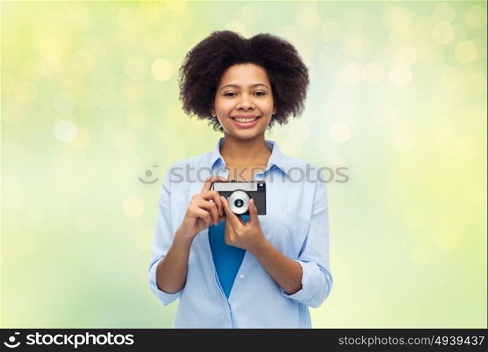 people and photography portrait concept - happy african american young woman with film camera over summer green lights background. happy african american woman with film camera