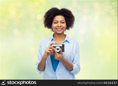 people and photography portrait concept - happy african american young woman with film camera over summer green lights background. happy african american woman with film camera